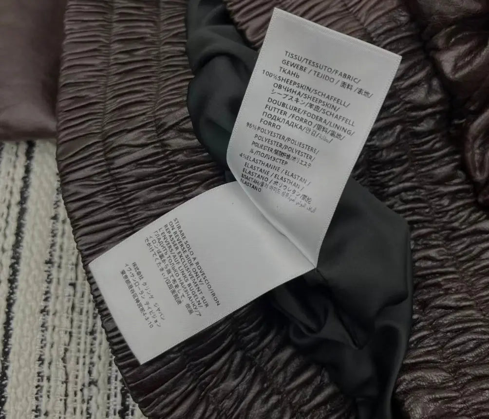 Close-up of a dark brown crinkled fabric garment with two white care labels attached, showing product details in German and Japanese.