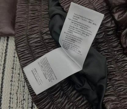 Close-up of a dark brown crinkled fabric garment with two white care labels attached, showing product details in German and Japanese.