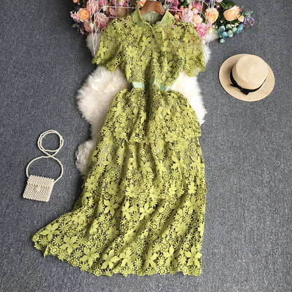 Green lace dress on a gray surface with a hat and handbag nearby