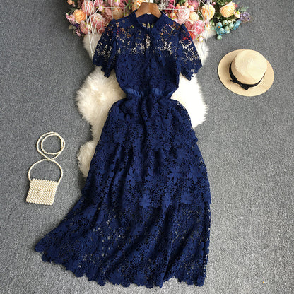 Navy blue lace dress on a gray surface with a straw hat and small bag.