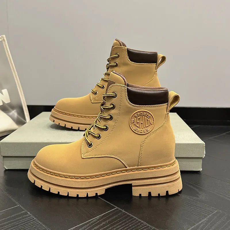 A pair of tan lace-up ankle boots with dark brown trim and a chunky lug sole, displayed on a light gray shoe box against a neutral gray background.