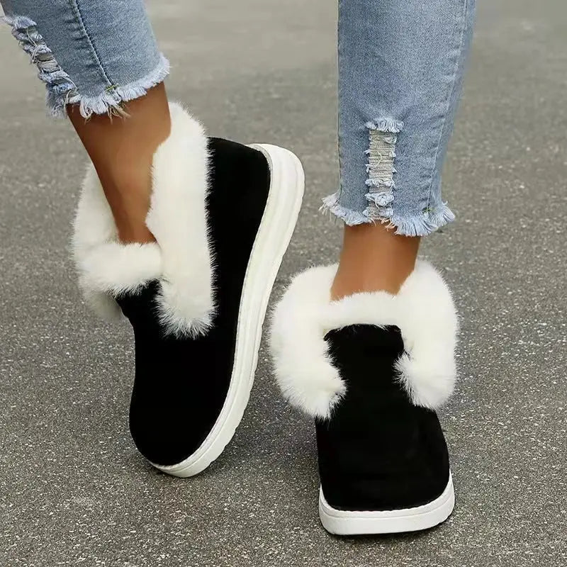 Black slip-on shoes with white fur trim worn with light blue jeans on a gray pavement.