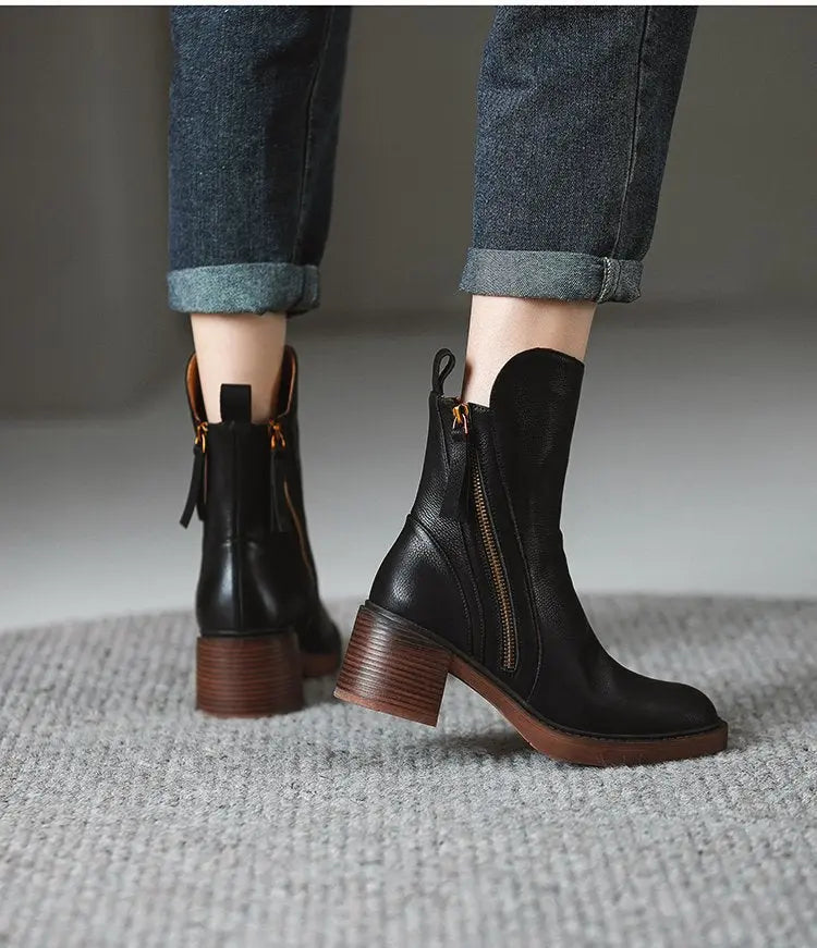 Black leather boots with brown soles worn with rolled-up jeans on a neutral background
