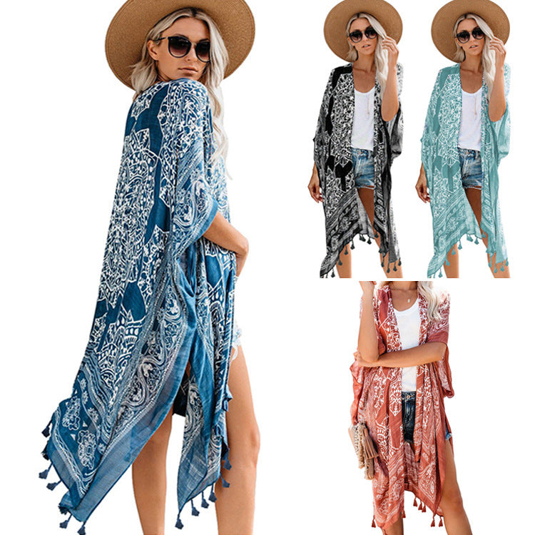 Woman wearing a patterned boho kimono-style cover-up in blue, paired with a wide-brimmed hat, white top, and denim shorts. Smaller images feature the same cover-up in black, teal, and rust colors—elegant, flowy, and perfect for layering.