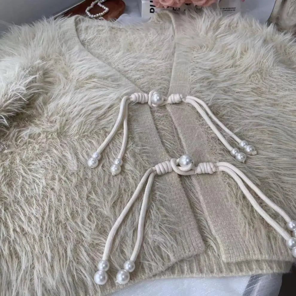 A close-up of a cream-colored faux fur cardigan featuring traditional Chinese-style cord and pearl closures on the front.