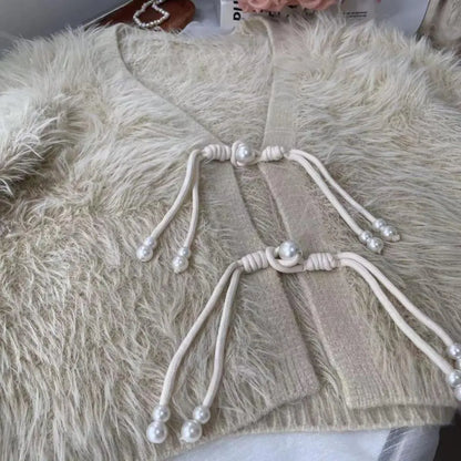 A close-up of a cream-colored faux fur cardigan featuring traditional Chinese-style cord and pearl closures on the front.