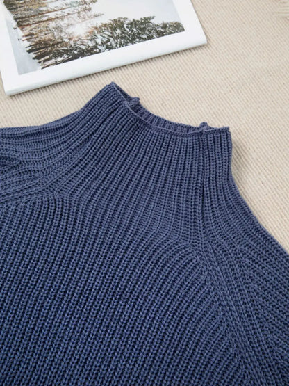 Close-up of a navy blue ribbed knit sweater laid flat on a beige textured surface, with a framed picture partially visible in the top corner.