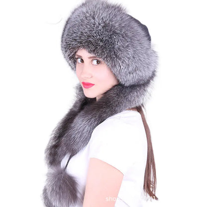 A woman wearing a large gray fur ushanka hat with a matching faux-fur neck warmer and pom-pom, photographed against a plain white background.