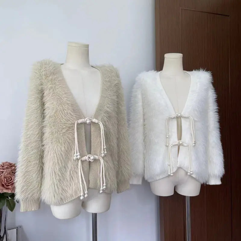 Two fuzzy open-front cardigans displayed on mannequins indoors. The left cardigan is a light beige/cream shaggy texture with cream cord and bead closures.