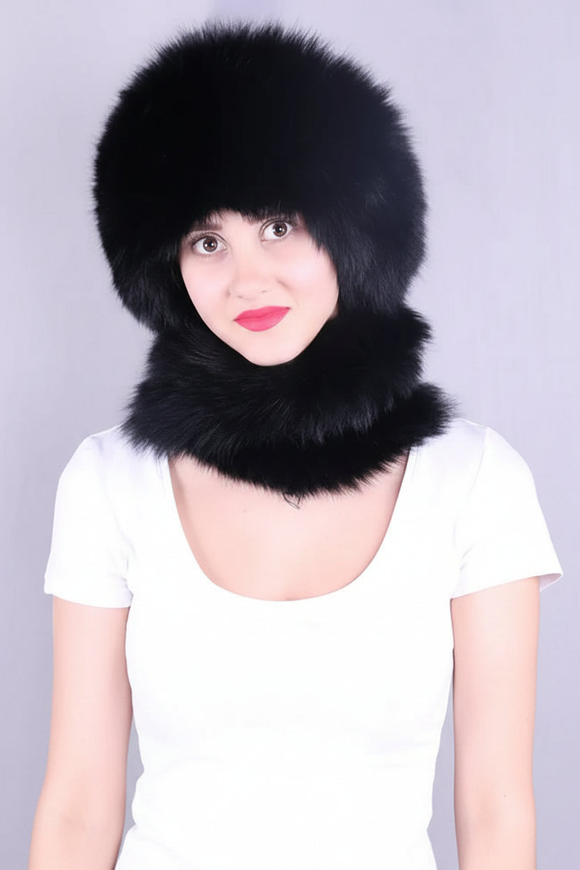 A woman wearing a black fur winter hat with an integrated neck warmer, photographed against a plain light gray background. The brand name 'Joolsana' is visible in the top left corner.