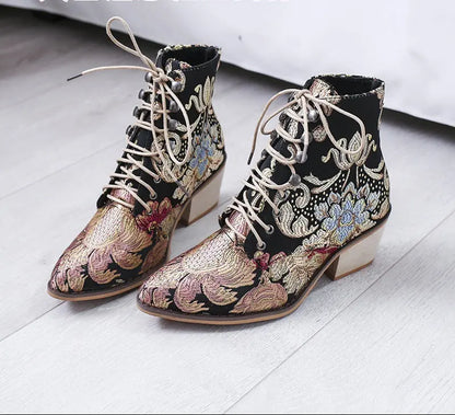 Pair of black embroidered boots with floral patterns on a light wooden floor.