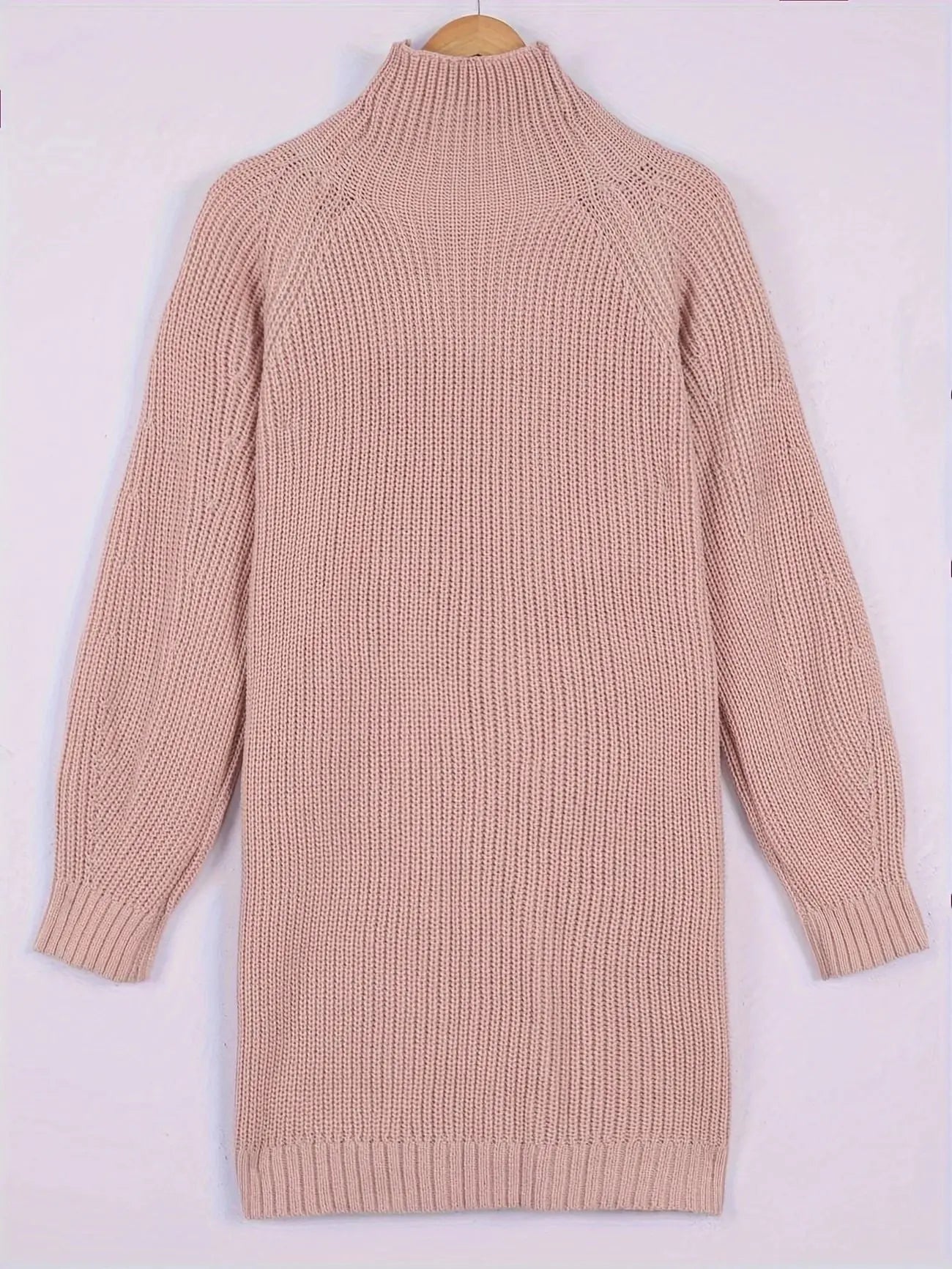 A light pink ribbed knit turtleneck sweater dress with long raglan sleeves, shown hanging on a wooden hanger against a plain light background.