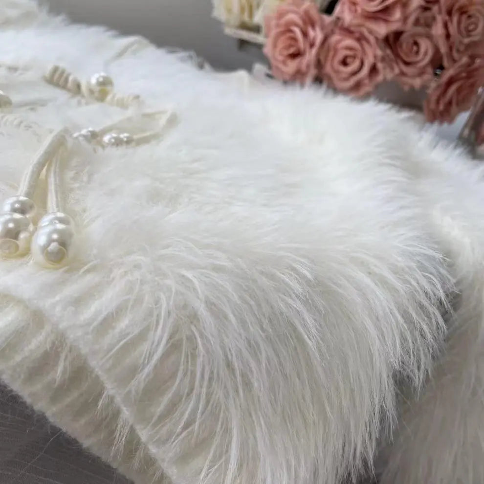 White faux fur blanket with pearl bead tassels and decorative pink roses in the background.