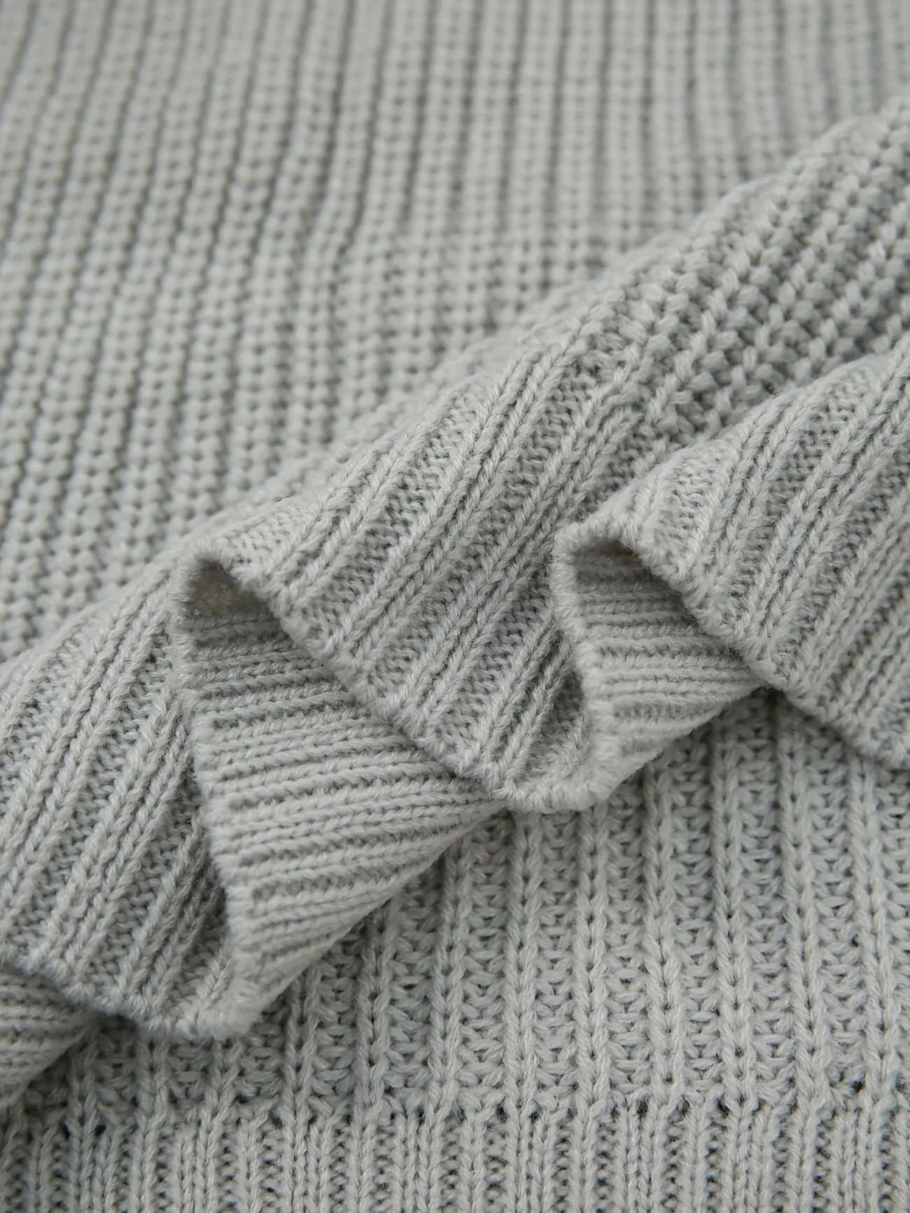 Close-up of a light gray ribbed knit fabric with soft folds showing the texture and weave.