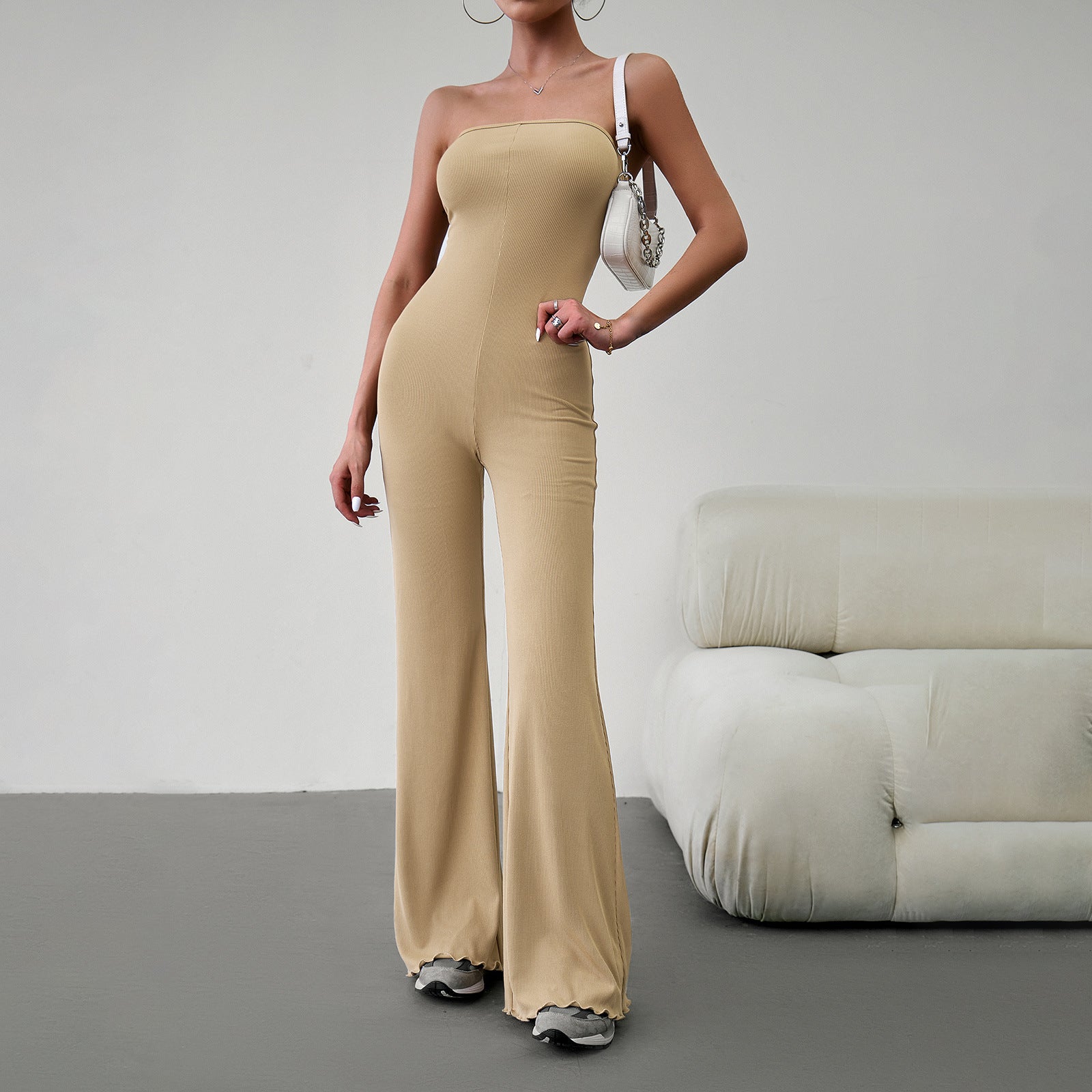 Elegant strapless jumpsuit available in beige, blue, brown, light beige, and black – form-fitting with a flared bottom, paired with sneakers and a white handbag.