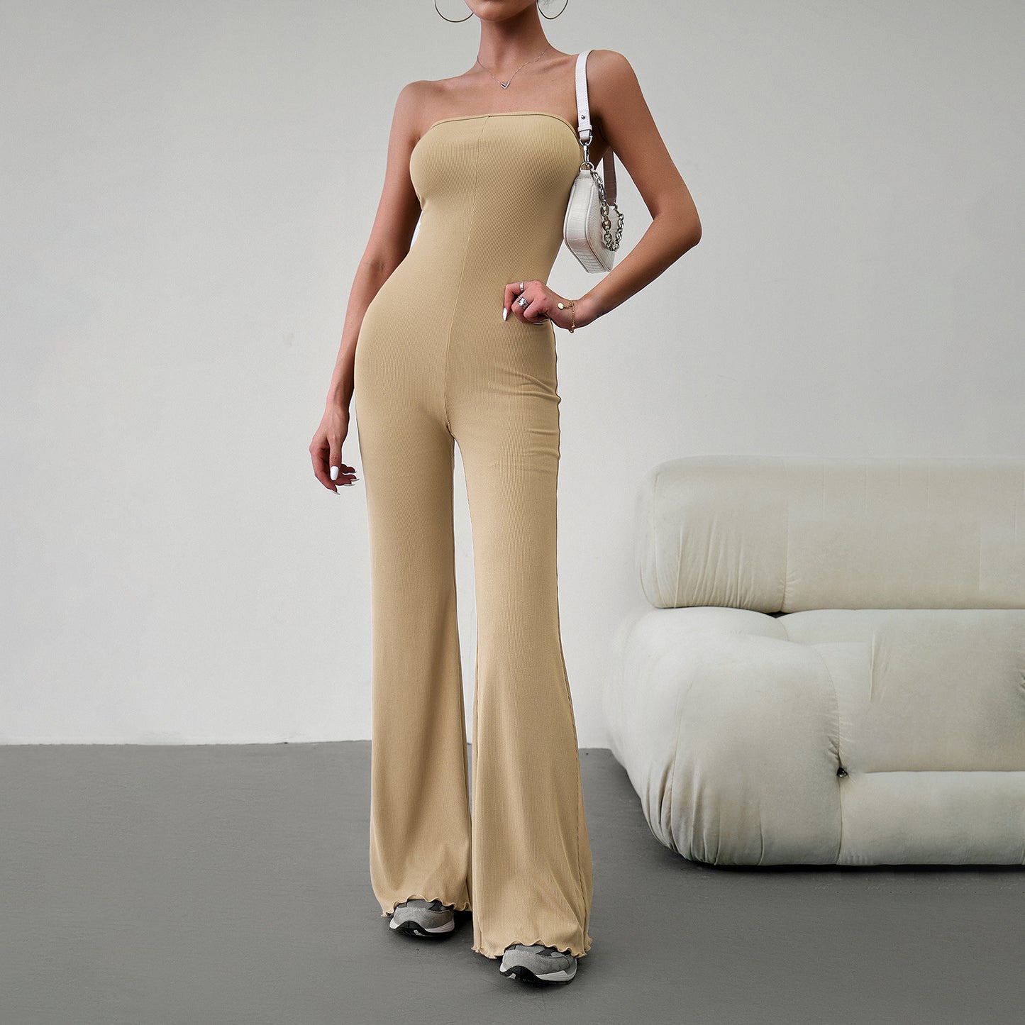Elegant strapless jumpsuit available in beige, blue, brown, light beige, and black – form-fitting with a flared bottom, paired with sneakers and a white handbag.