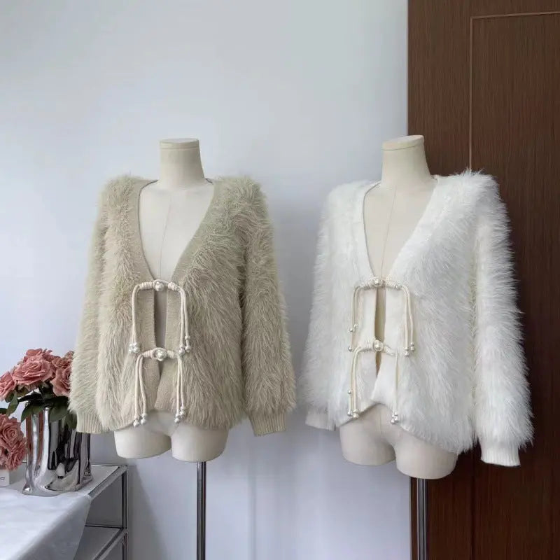 Two fuzzy open-front cardigan-style jackets displayed on mannequins indoors. The left jacket is a light oatmeal beige, and the right jacket is white.