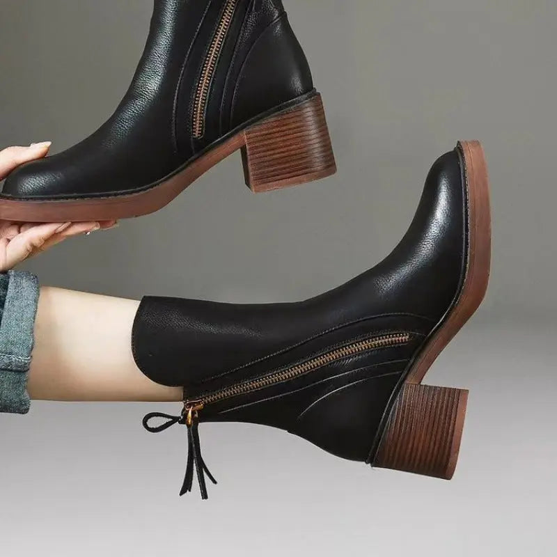 Black leather ankle boots with brown soles worn by a person on a gray background