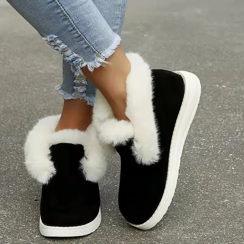 Black slip-on shoes with white fur trim worn with light blue jeans on a gray pavement.