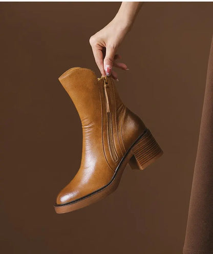 Brown leather ankle boot held by a hand against a brown background