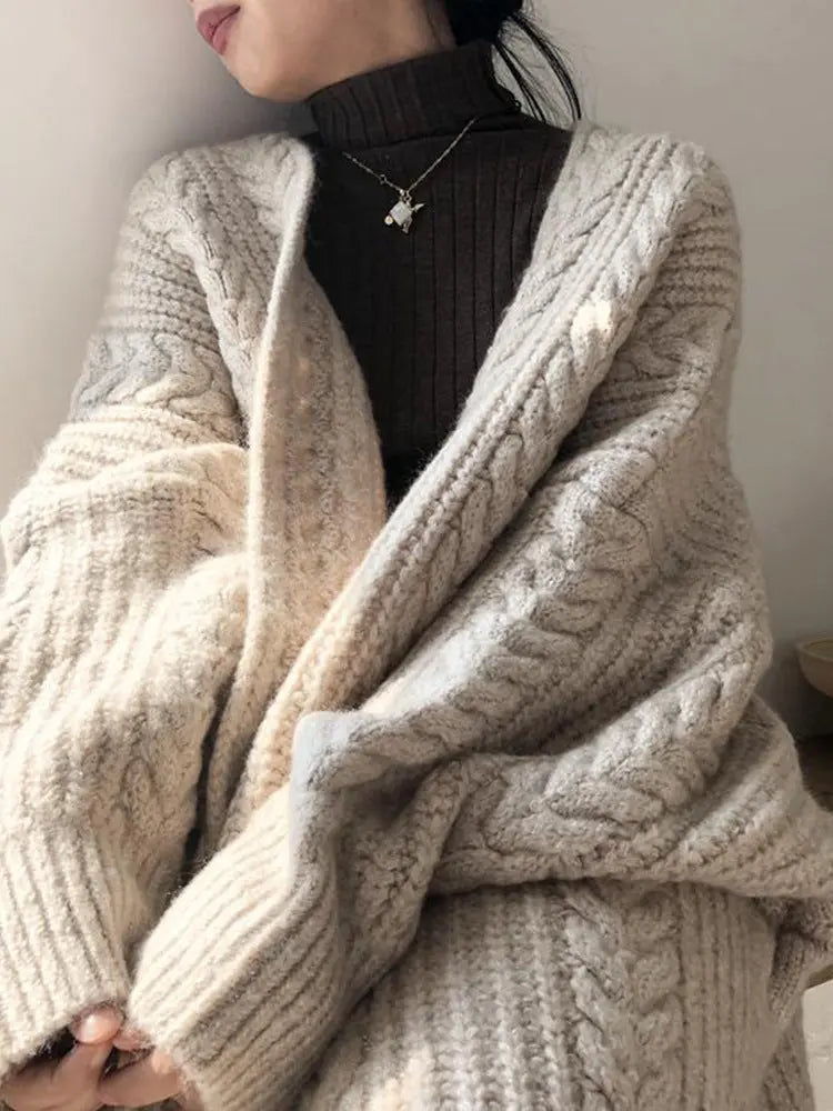 Person wearing a beige knitted cardigan over a black turtleneck against a neutral background