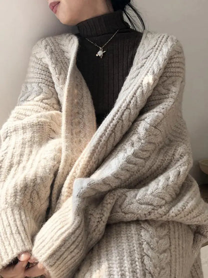 Person wearing a beige knitted cardigan over a black turtleneck against a neutral background