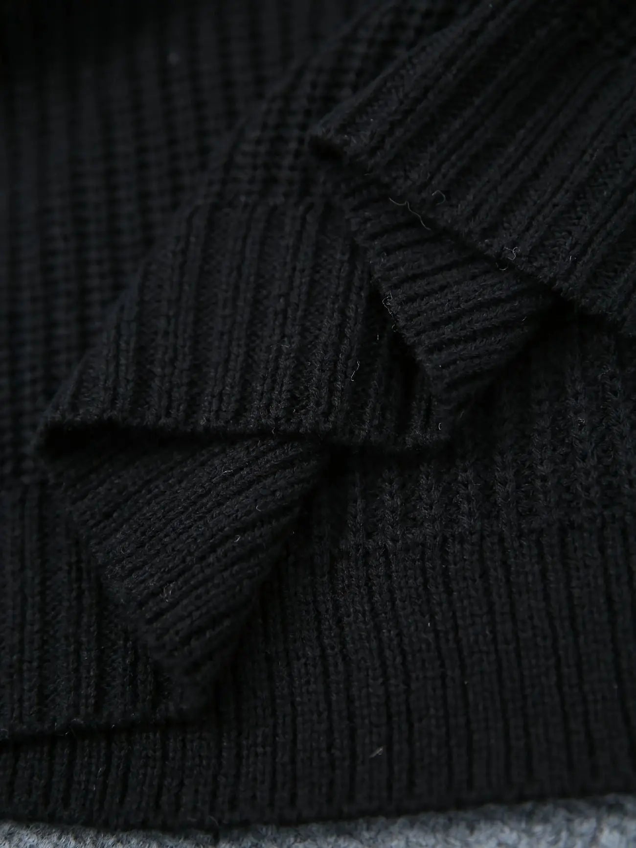 Close-up of a black ribbed knit fabric, showing the detailed texture and folds of the material.