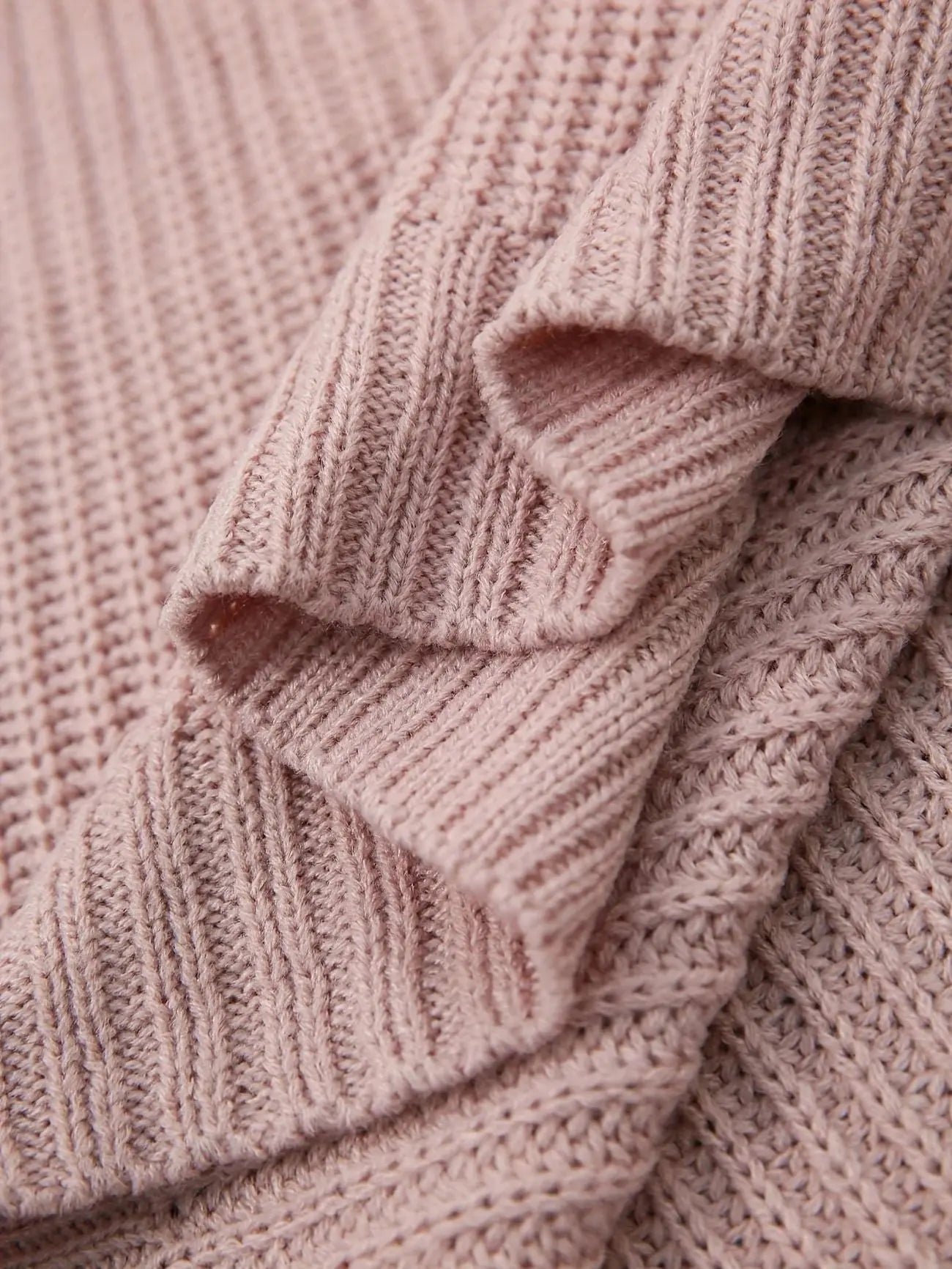 Close-up of a dusty pink ribbed knit fabric with layered draped folds showing the soft texture and stitch detail.