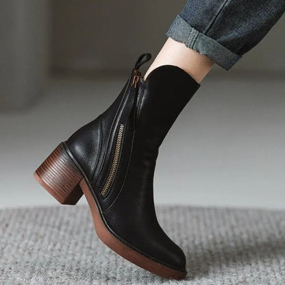 Black ankle boot with brown sole worn by a person on a neutral background