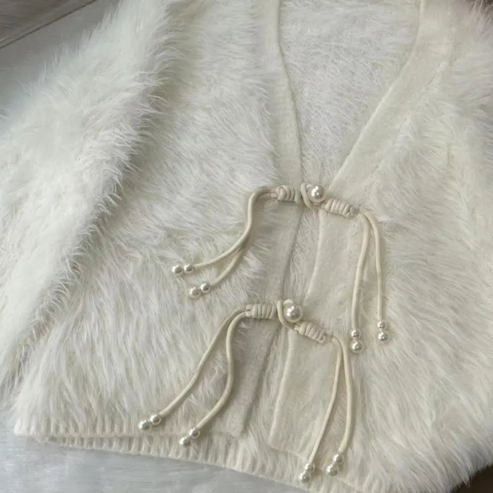 A close-up of a fluffy cream faux-fur garment with a V-neck and drawstring closures adorned with pearl-like beads.