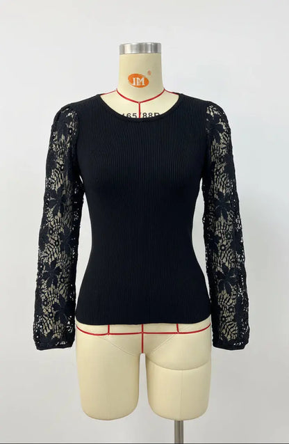 A black long-sleeve ribbed knit top with black lace sleeves, displayed on a beige mannequin torso against a white wall with framed cityscape prints.