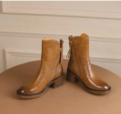 Pair of brown leather ankle boots on a beige surface with a neutral background