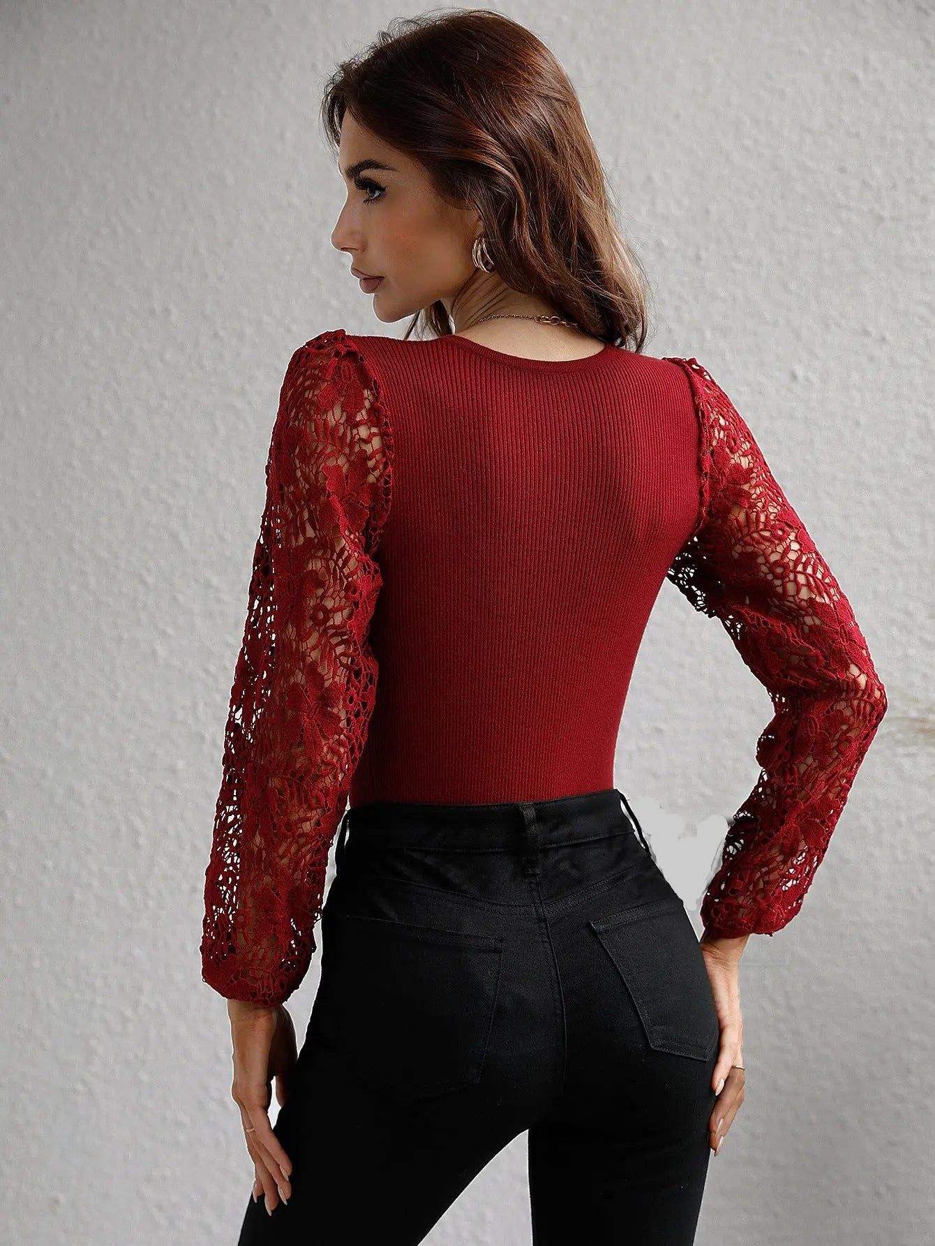 Woman wearing a red top with lace sleeves against a gray background
