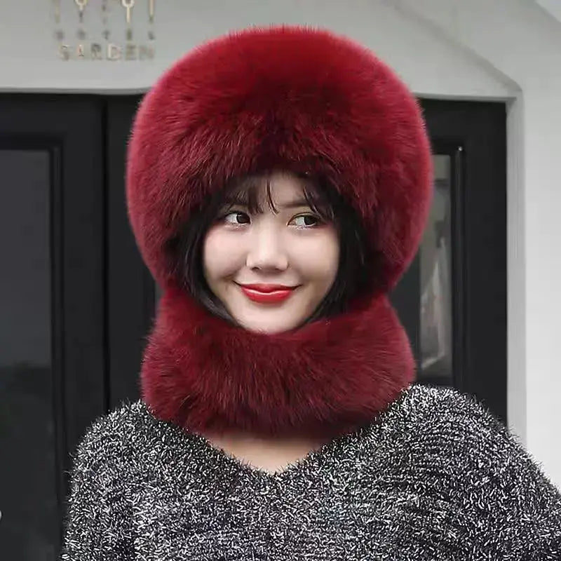 A woman wearing a luxurious deep red fur winter hat with an integrated neck warmer and a matching fluffy pom-pom, paired with a sparkly gray sweater.