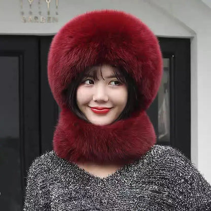 A woman wearing a luxurious deep red fur winter hat with an integrated neck warmer and a matching fluffy pom-pom, paired with a sparkly gray sweater.