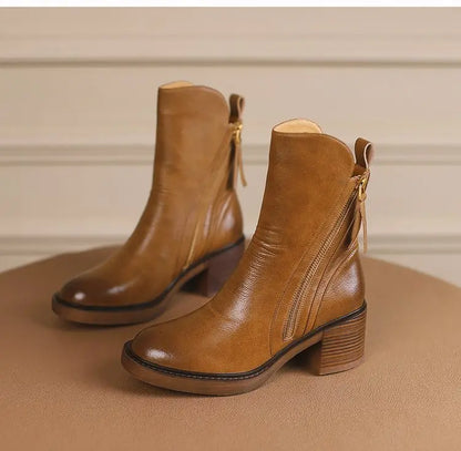 Pair of brown leather ankle boots on a beige surface with a neutral background