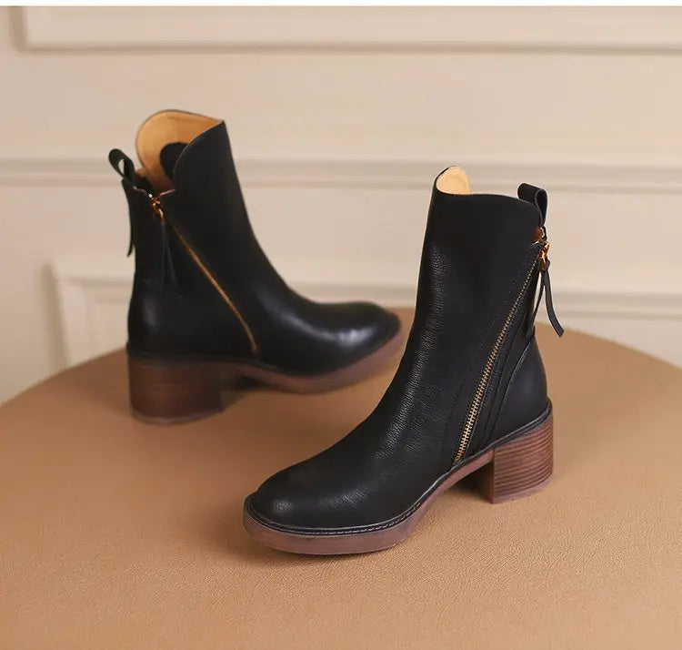 Black leather ankle boots with brown soles on a beige surface