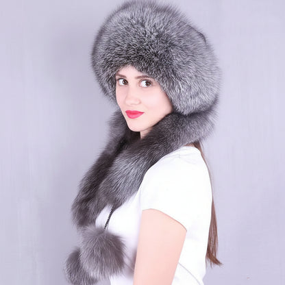 A woman wearing a large gray fur hat with matching fur trim and a matching fur neck warmer, photographed against a plain light gray background. The brand name 'Joelsana' appears in the upper left corner.