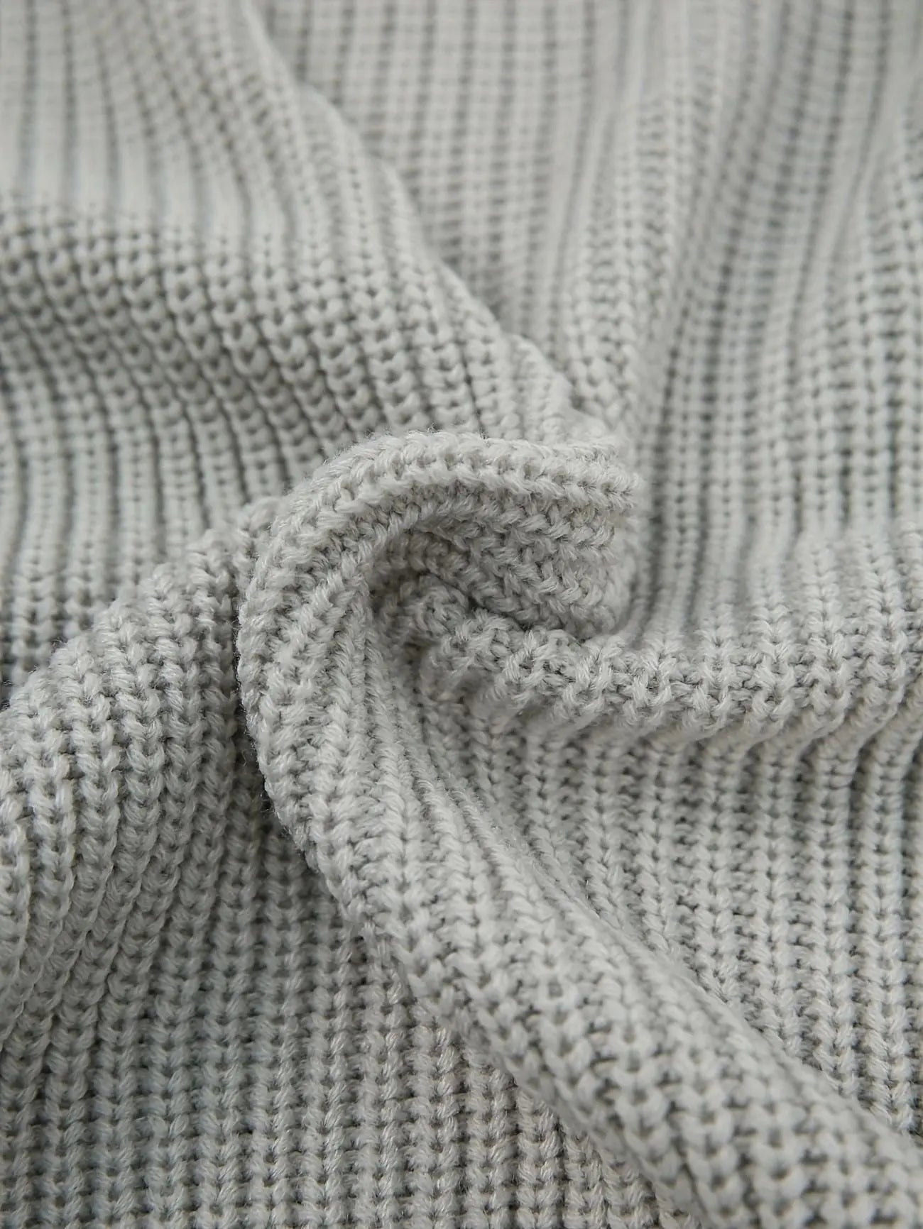 Close-up of a light gray ribbed knit fabric with a soft, draped texture.
