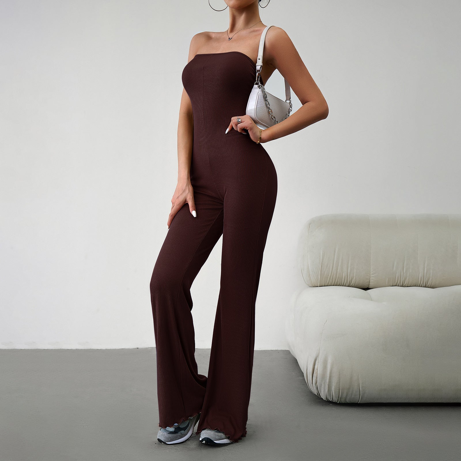 Elegant strapless jumpsuit available in beige, blue, brown, light beige, and black – form-fitting with a flared bottom, paired with sneakers and a white handbag.