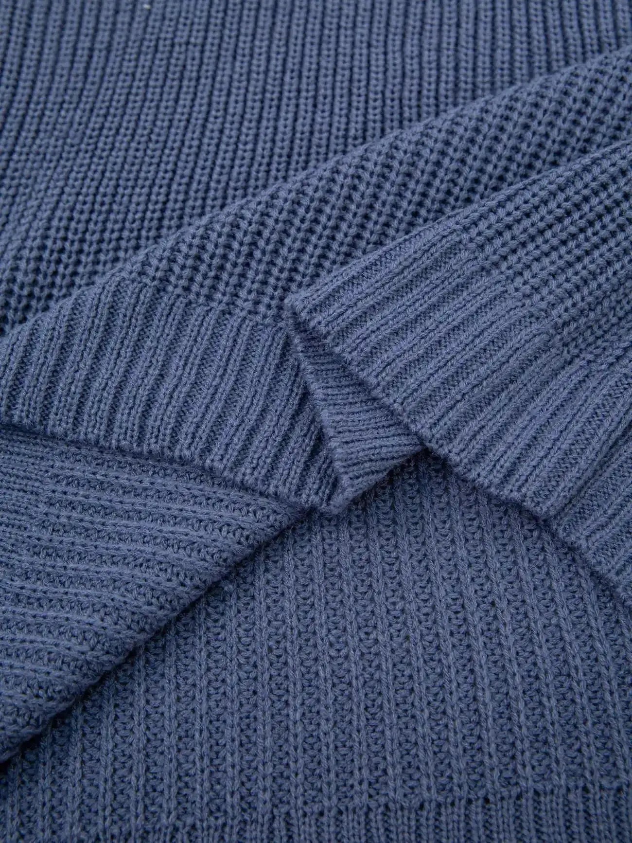 Close-up of a textured knit fabric in a muted slate blue color, showing the ribbed pattern and folded layers.