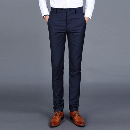 Multiple views of structured tailored trousers in navy, grey, black, and additional colours, styled with a white shirt and brown shoes, highlighting pleats, tapered legs, and buttoned back pockets

