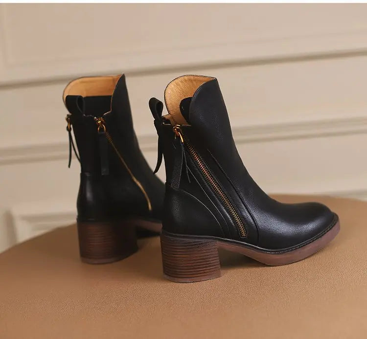 Black ankle boots with brown soles on a beige surface