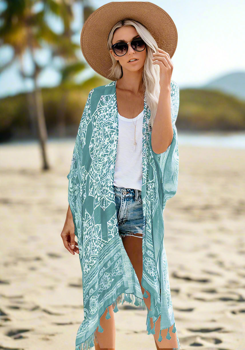 Woman wearing a patterned boho kimono-style cover-up in blue, paired with a wide-brimmed hat, white top, and denim shorts. Smaller images feature the same cover-up in black, teal, and rust colors—elegant, flowy, and perfect for layering.