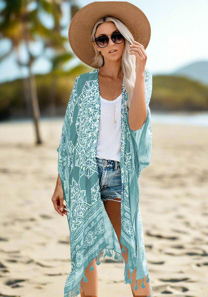 Woman wearing a patterned boho kimono-style cover-up in blue, paired with a wide-brimmed hat, white top, and denim shorts. Smaller images feature the same cover-up in black, teal, and rust colors—elegant, flowy, and perfect for layering.