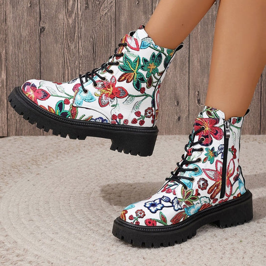 White combat-style boots with a vibrant floral pattern, black laces, deep-tread black soles, and side zippers—bold, stylish, and perfect for any outfit.
