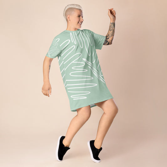 Light green oversized t-shirt dress featuring white abstract line patterns, worn with black sneakers—modern, artistic, and perfect for casual street-style fashion.