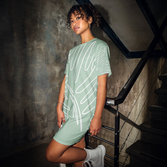 Light green oversized t-shirt dress featuring white abstract line patterns, worn with white sneakers, standing on an industrial staircase—modern, artistic, and perfect for casual street-style fashion.