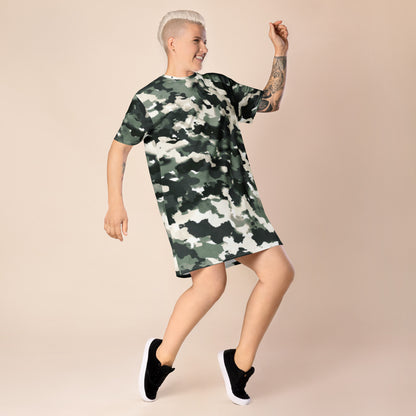 Person wearing a camouflage-patterned t-shirt dress featuring green, black, and white shades, paired with black sneakers with white soles—stylish, sporty, and perfect for casual streetwear.