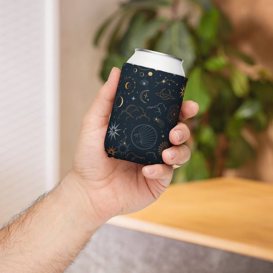 Hand holding a black can cooler with celestial-themed prints in gold and white—featuring stars, planets, clouds, and an eye, wrapped around a slim can—stylish, insulated, and available in two sizes.
